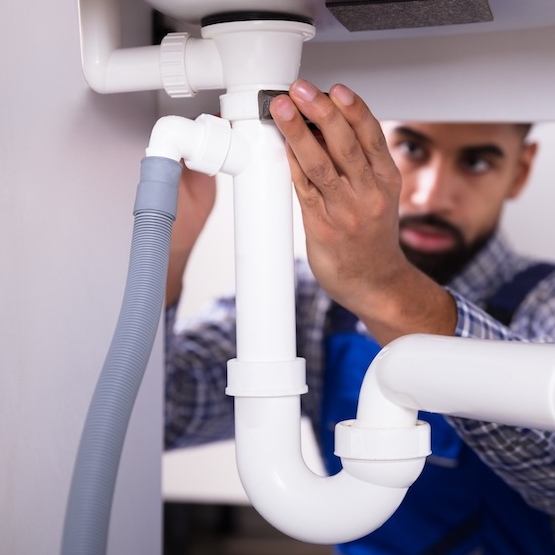 An experienced plumber is installing PVC pipes underneath a sink.